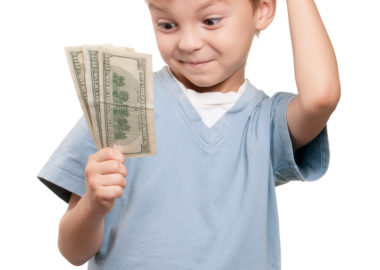 Portrait of a surprised little boy holding a dollars over white background
