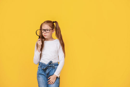 Little girl with magnifying glass on color background